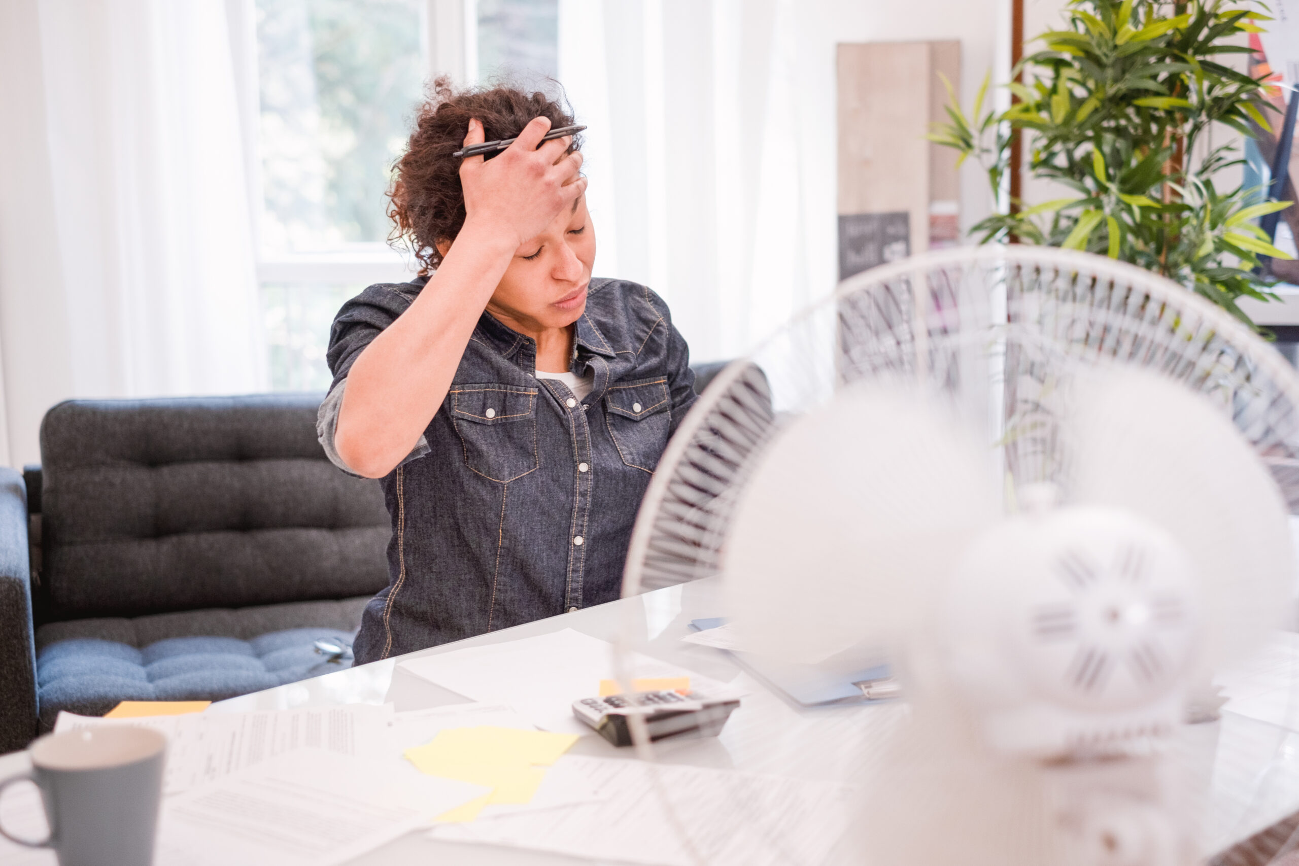 Overheated woman using a fan at her desk during a summer heatwave at home